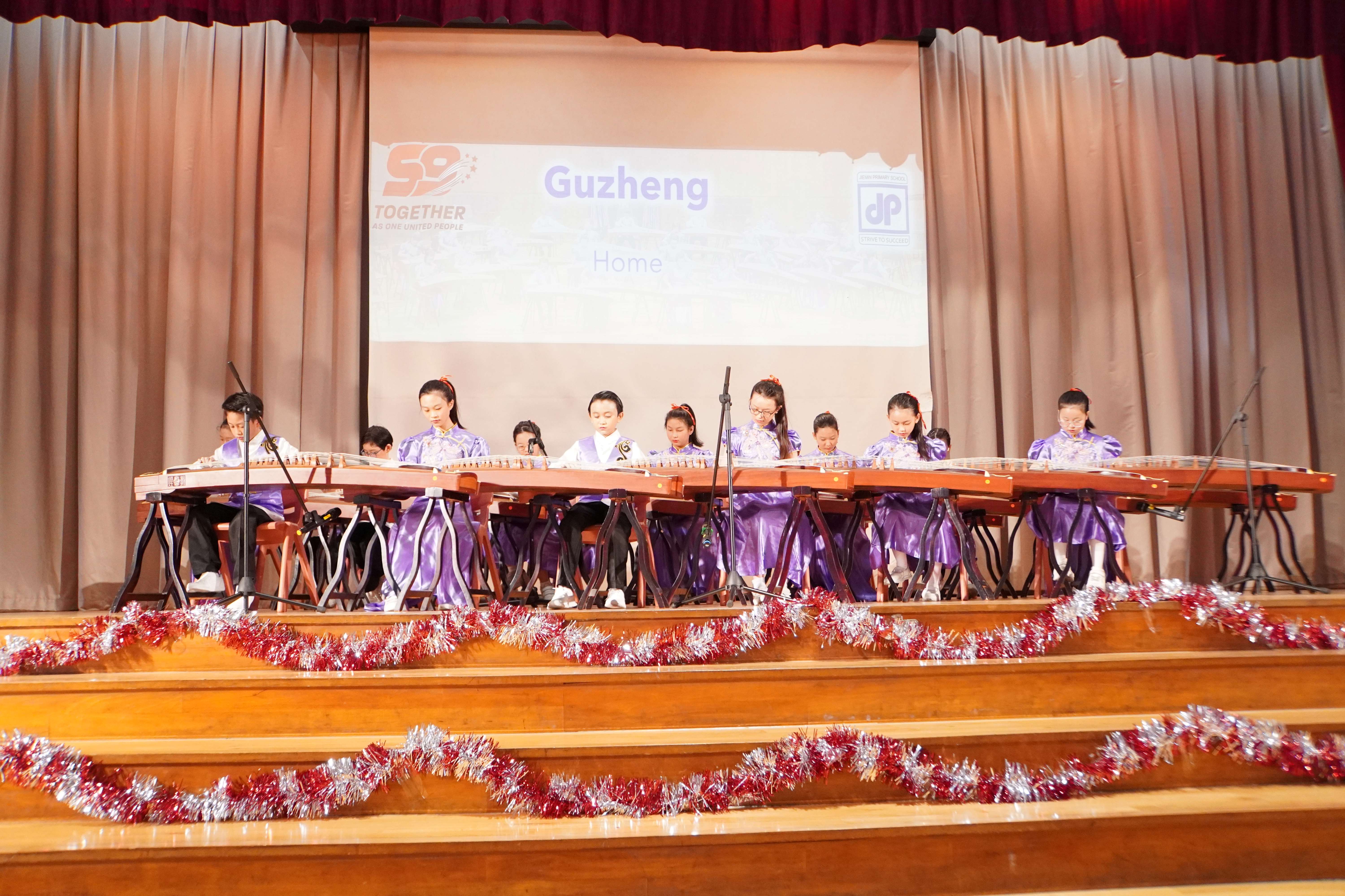 Students in purple costumes perform together on guzhengs on stage.